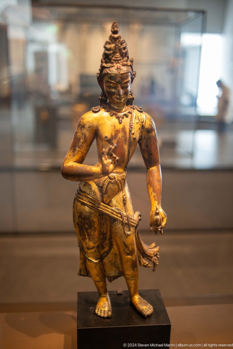 Gilded standing figure with raised arm at Louvre Abu Dhabi.