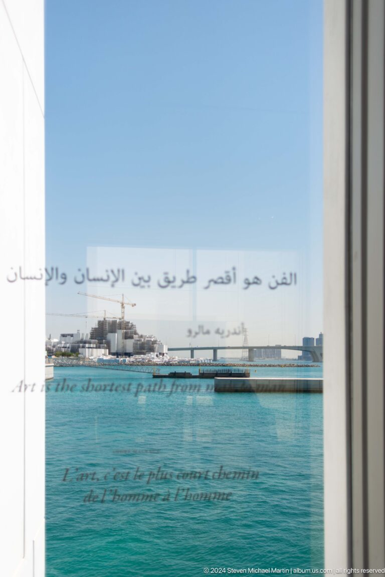 Bilingual quotation on glass overlooking water at Louvre Abu Dhabi.