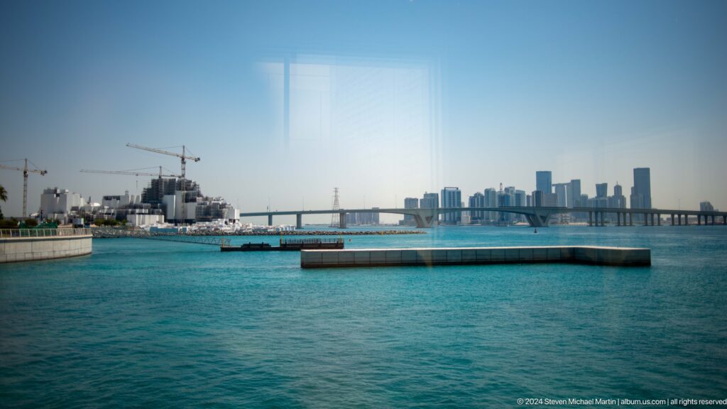 Turquoise waterfront and distant city skyline at Louvre Abu Dhabi.