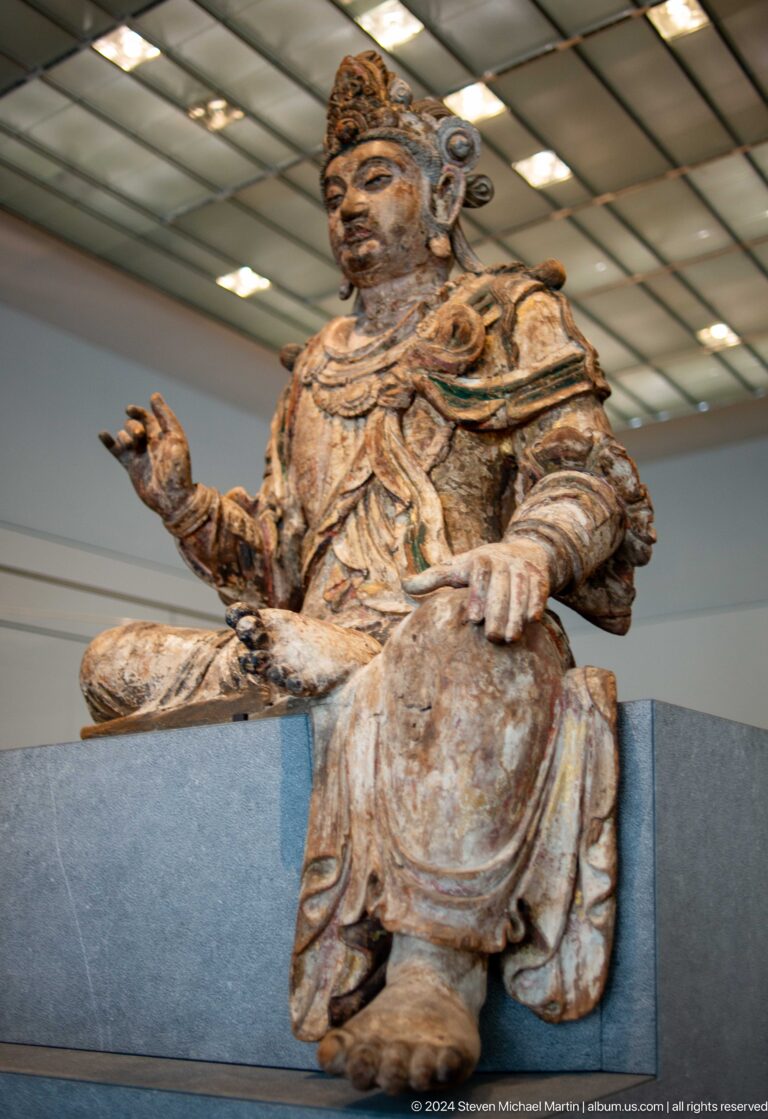 Large seated bearded sculpture holding object at Louvre Abu Dhabi.
