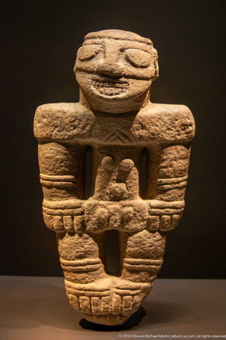 Stone figure framed by massive hands and architectural form at Louvre Abu Dhabi.