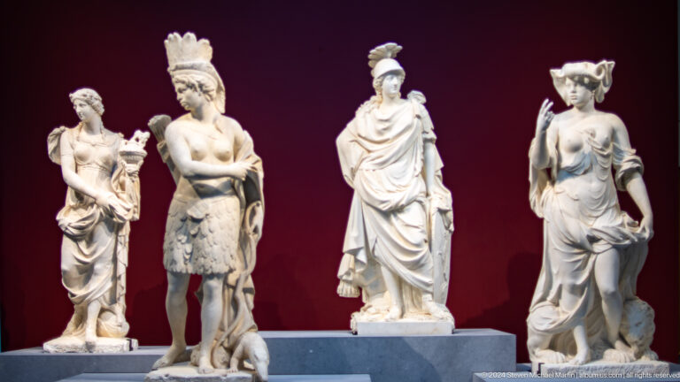 Group of classical marble statues against red wall at Louvre Abu Dhabi.