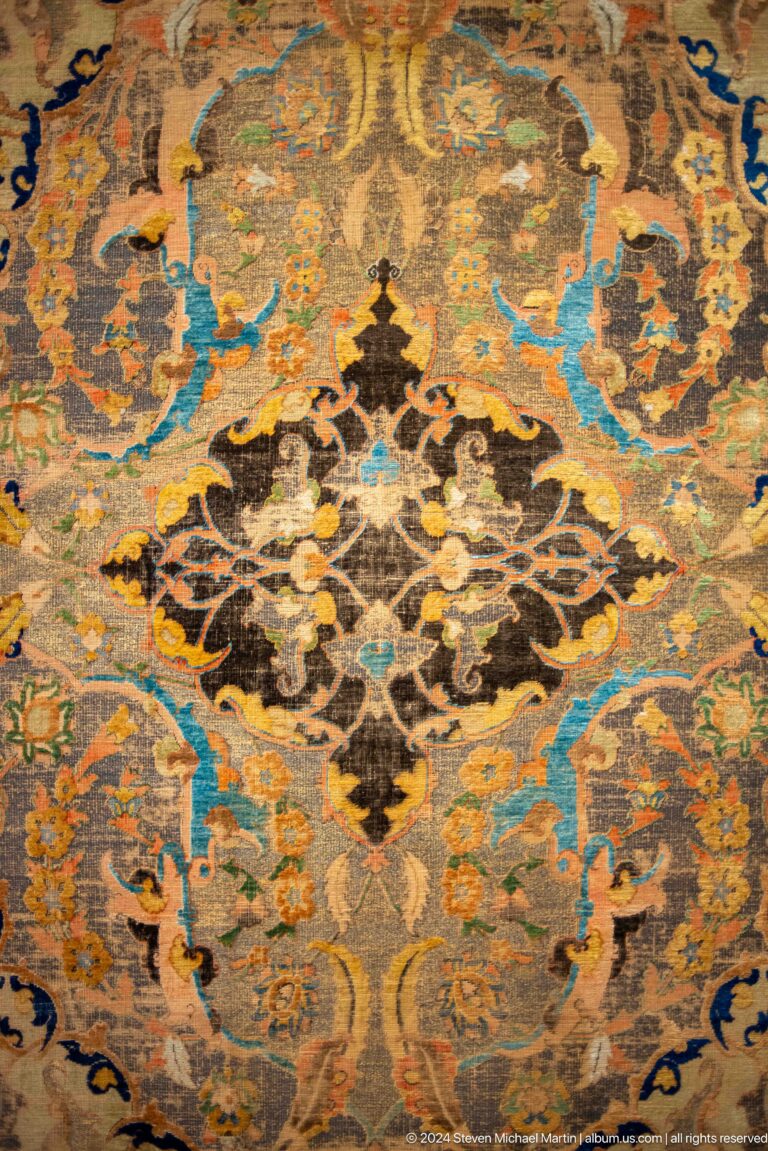 Ornate textile with central black floral medallion at Louvre Abu Dhabi.