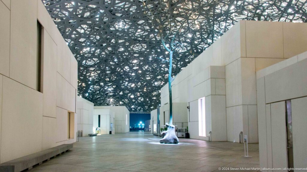Broad passage between white galleries under dome at Louvre Abu Dhabi.