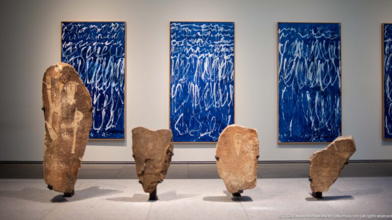 Gallery installation of stone fragments before blue panels at Louvre Abu Dhabi.