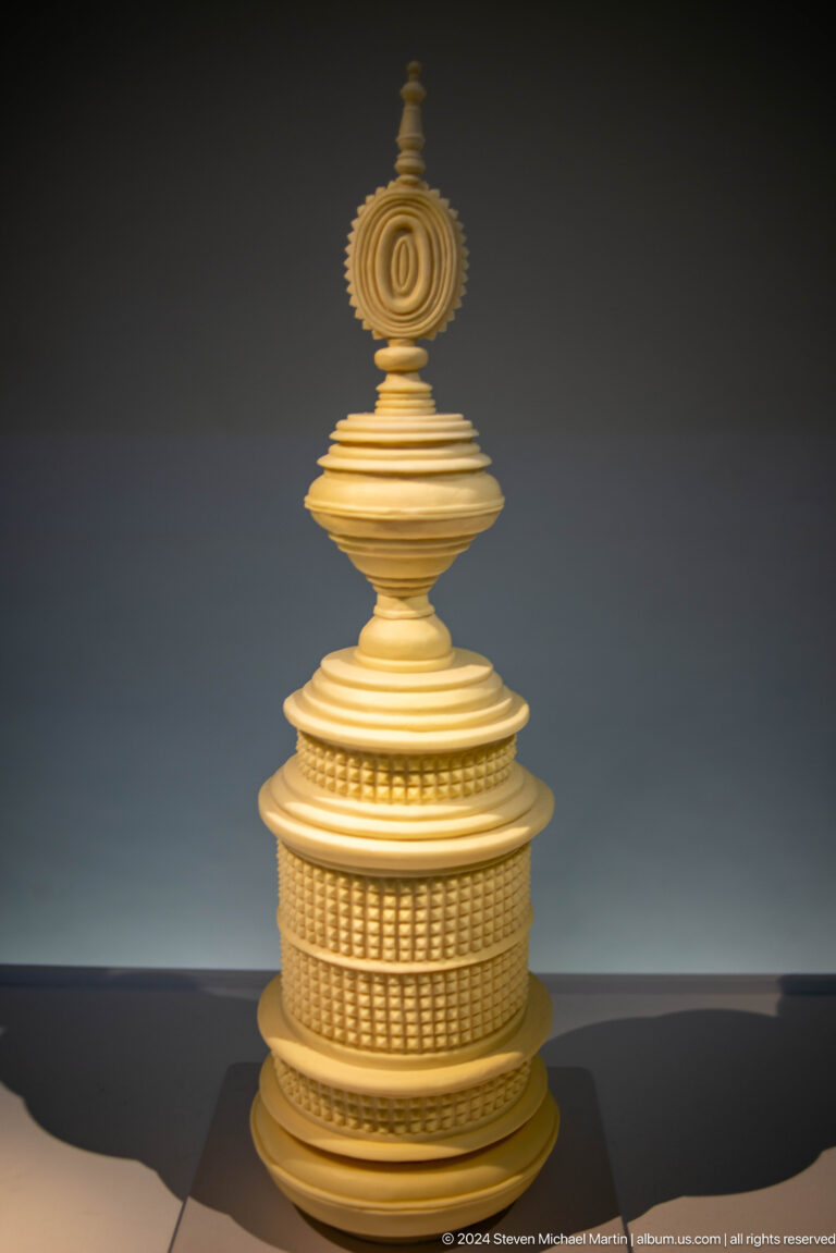 Gold tiered finial against gray background at Louvre Abu Dhabi.