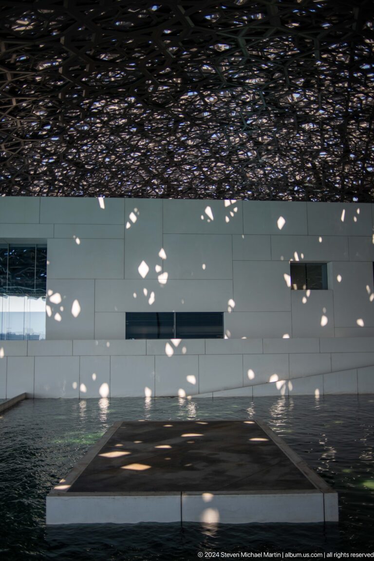 Scattered light spots across white gallery wall at Louvre Abu Dhabi.