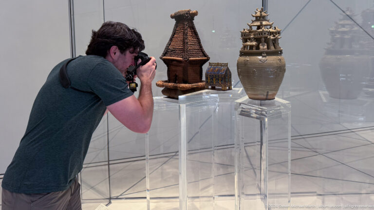 Visitor photographing tall historic vessels at Louvre Abu Dhabi.