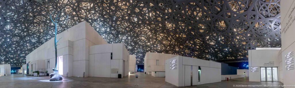 Museum galleries beneath perforated dome at night at Louvre Abu Dhabi.