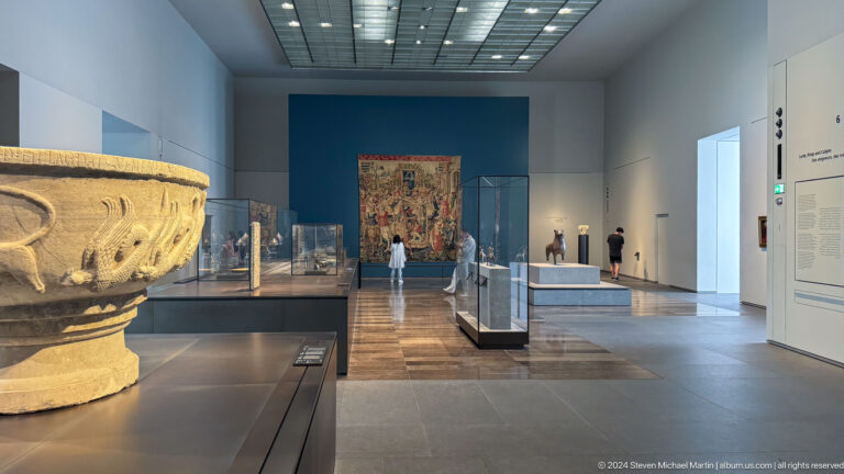 Wide gallery view with display cases and architectural fragments at Louvre Abu Dhabi.