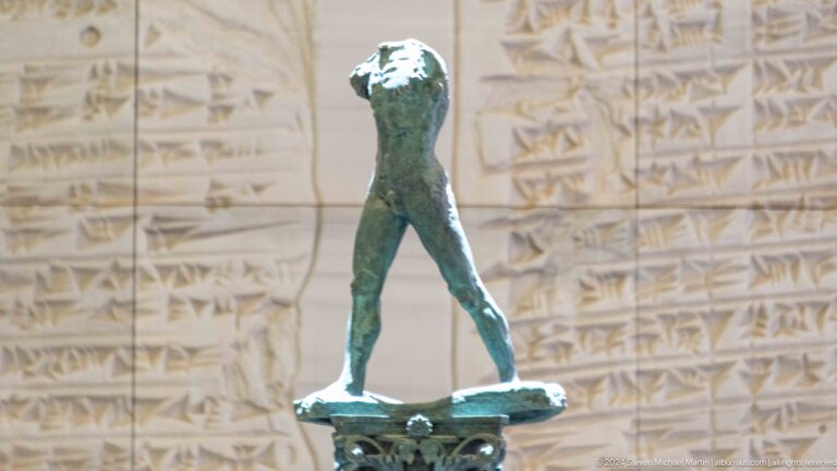 Small bronze walking figure before cuneiform tablet image at Louvre Abu Dhabi.
