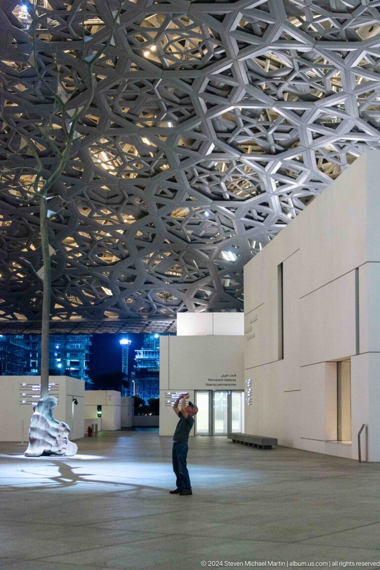 Museum galleries beneath layered metal canopy at Louvre Abu Dhabi.
