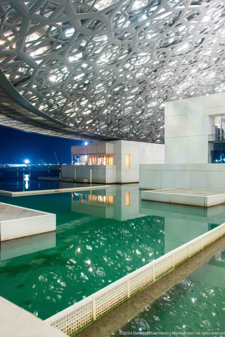 Reflecting pool beneath white gallery blocks at Louvre Abu Dhabi.