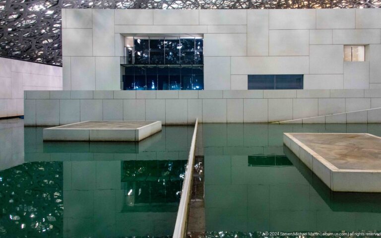 Green water channel between museum platforms at Louvre Abu Dhabi.