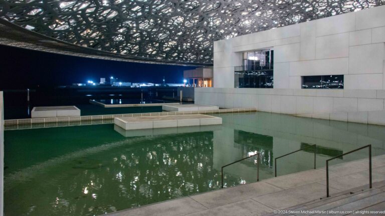 Large green reflecting pool beneath dome at Louvre Abu Dhabi.