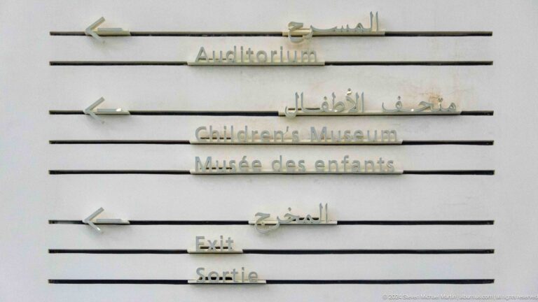 Multilingual gallery-direction sign at Louvre Abu Dhabi.