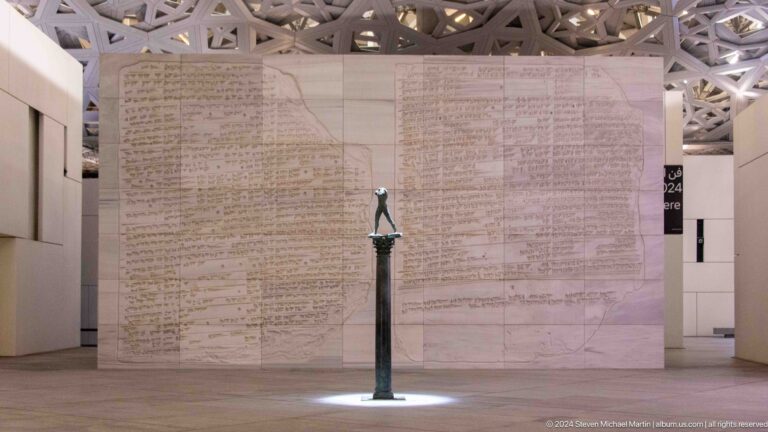Slender figure sculpture before patterned wall at Louvre Abu Dhabi.
