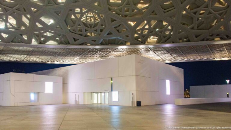 White galleries beneath dome at night at Louvre Abu Dhabi.