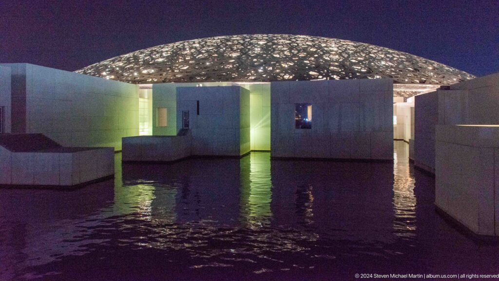 Museum galleries reflected in dark water at Louvre Abu Dhabi.