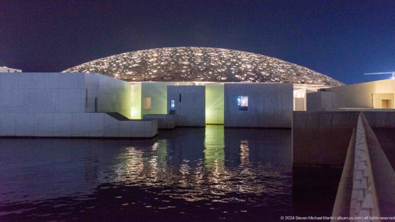 Illuminated museum dome reflected in water at Louvre Abu Dhabi.