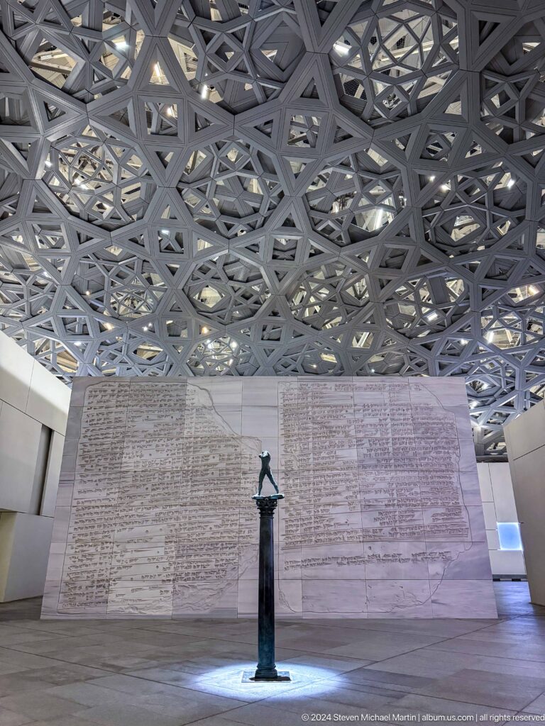 Sculpture on pedestal before patterned wall at Louvre Abu Dhabi.