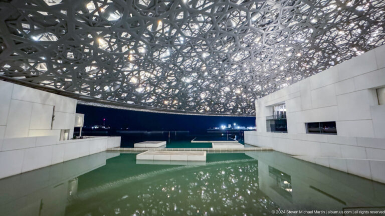 Broad green pool beneath patterned dome at Louvre Abu Dhabi.