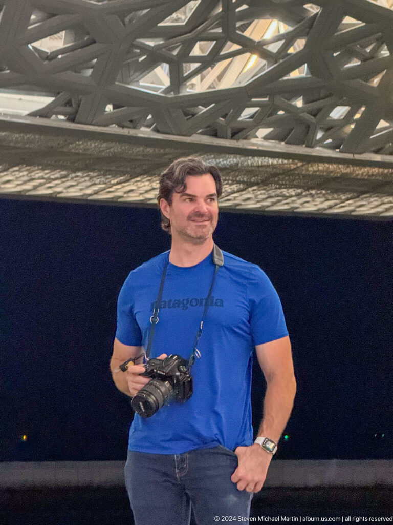 Portrait of visitor in blue shirt with camera strap at Louvre Abu Dhabi.