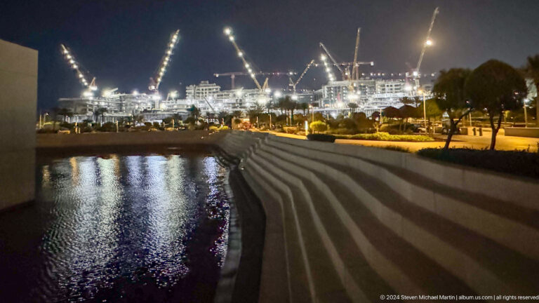 Waterfront promenade and construction lights at night at Louvre Abu Dhabi.