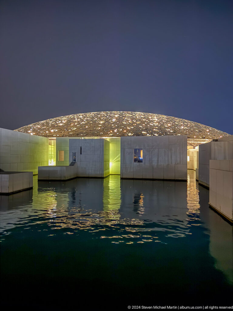 Museum galleries glowing above water at Louvre Abu Dhabi.