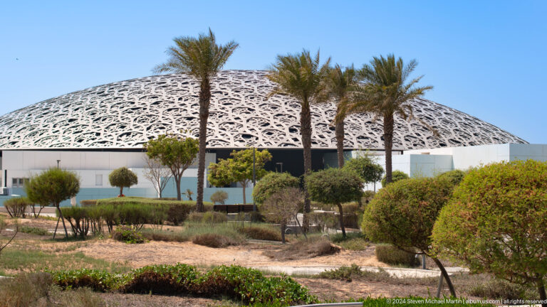 Museum dome rising behind palms and landscaped garden at Louvre Abu Dhabi.