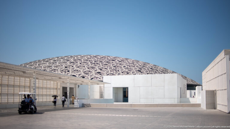 White museum buildings beneath dome in daylight at Louvre Abu Dhabi.