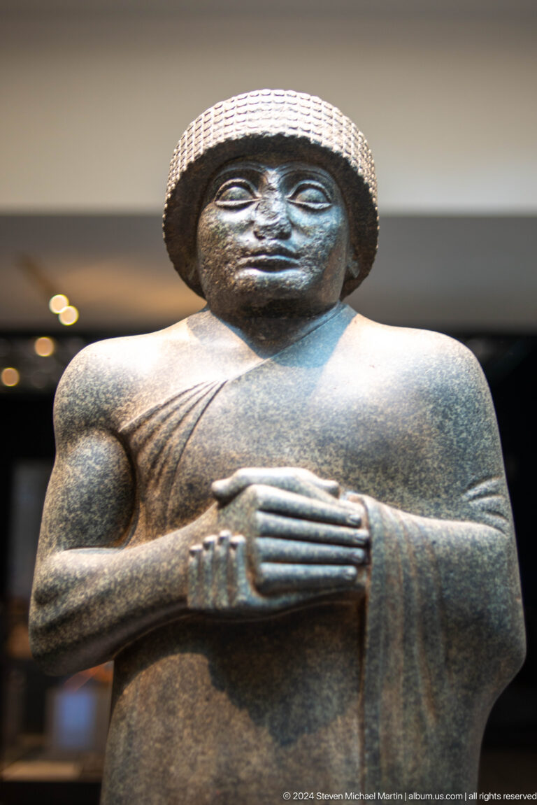 Dark stone seated figure with clasped hands at Louvre Abu Dhabi.