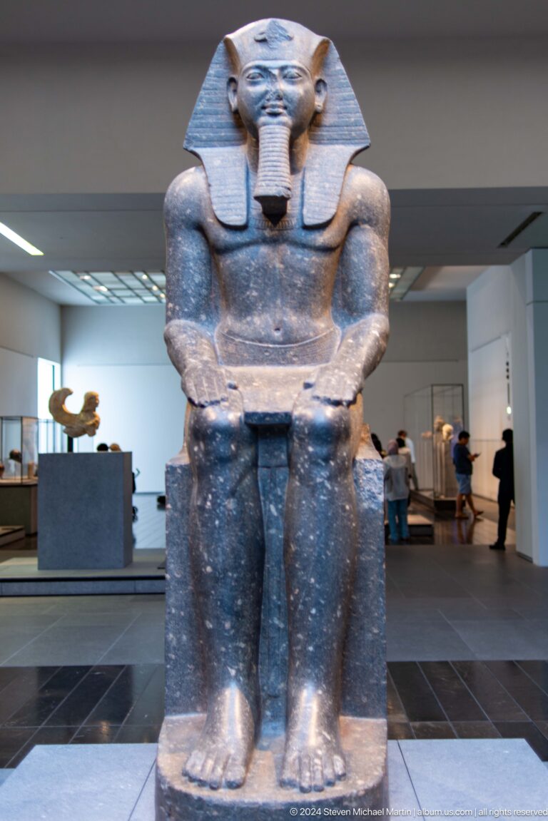 Monumental seated stone figure in gallery at Louvre Abu Dhabi.