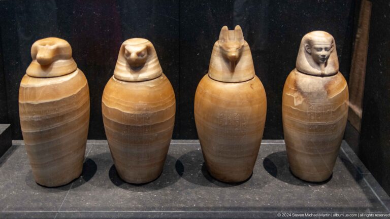 Row of four canopic jars with sculpted lids at Louvre Abu Dhabi.