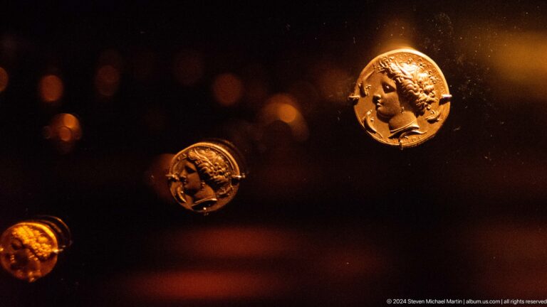 Gold coins displayed against dark background at Louvre Abu Dhabi.