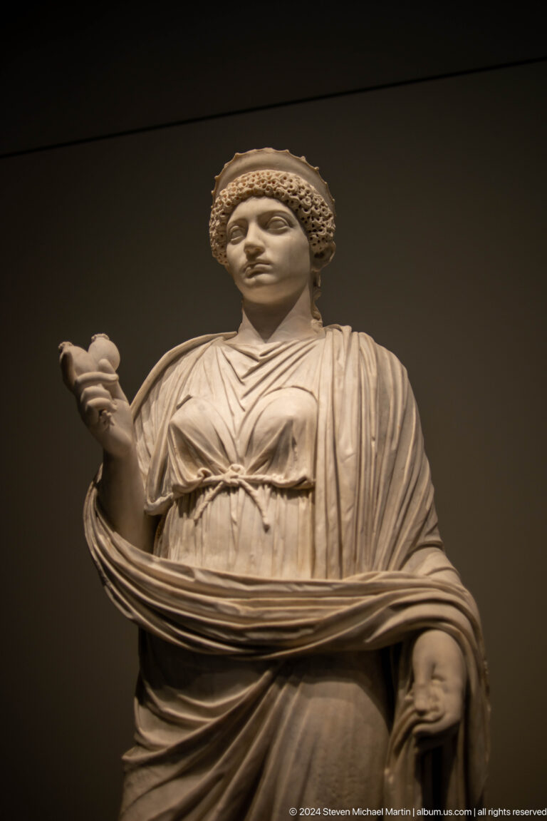 Standing marble woman holding a small figure at Louvre Abu Dhabi.