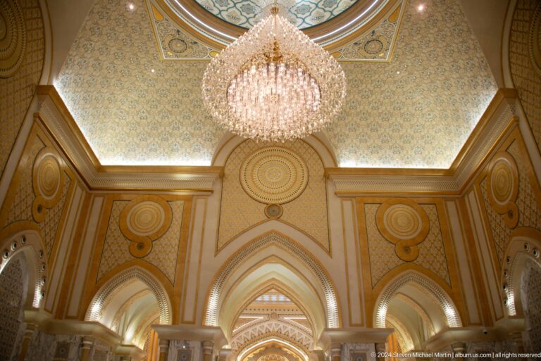 Crystal chandelier beneath gold-trimmed ceiling.