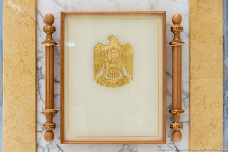 Framed uae emblem between carved wooden columns.
