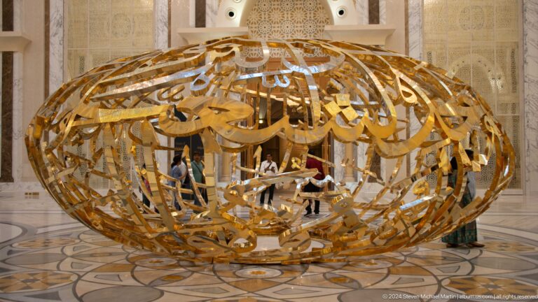Large gold calligraphic sculpture on polished floor.