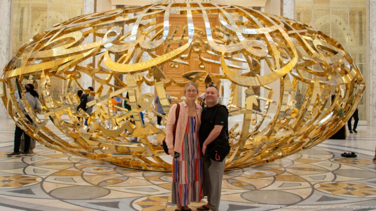 Two visitors posing in front of gold sculpture.