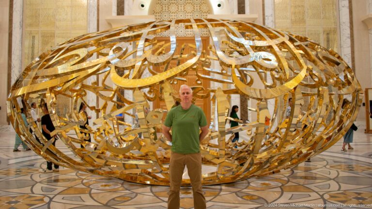 Visitor in green shirt before gold sculpture.