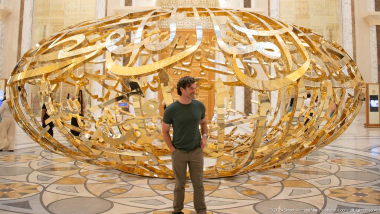 Visitor standing close to gold calligraphic sculpture.