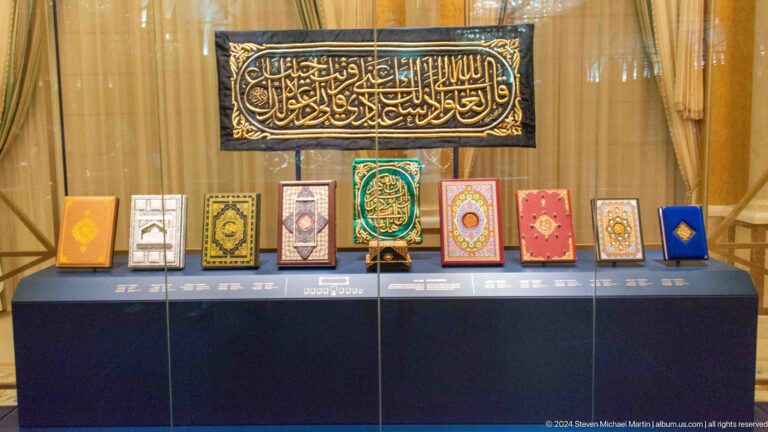 Display of qurans beneath arabic calligraphy panel.