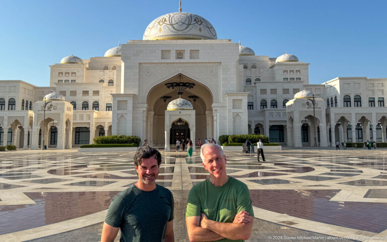 Two visitors posing before palace façade.