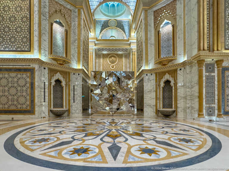 Ornate side hall with geometric floor and mirrored sculpture.