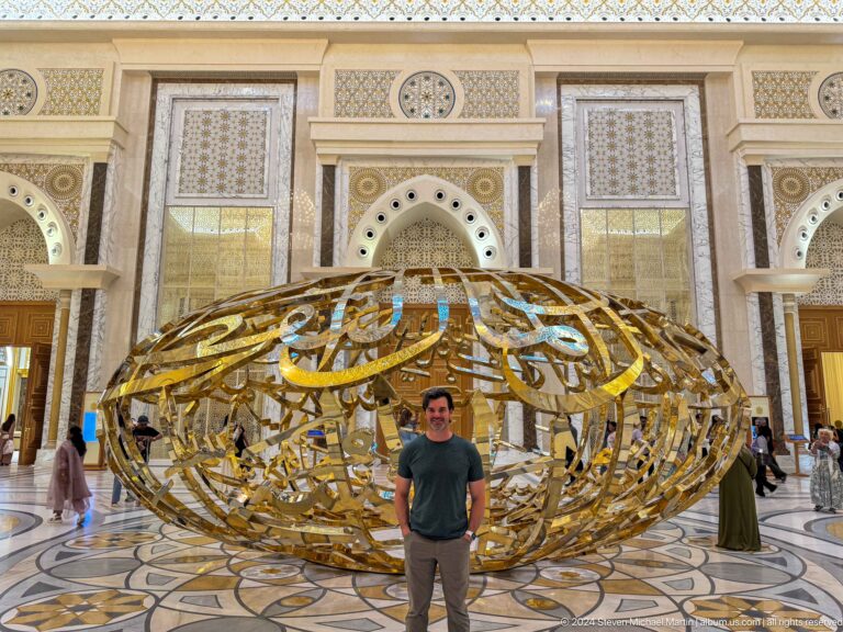 Visitor standing in front of gold calligraphic sculpture.