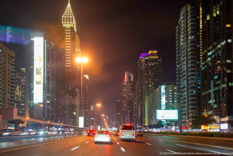 Night traffic on a Dubai boulevard lined with illuminated high-rises.