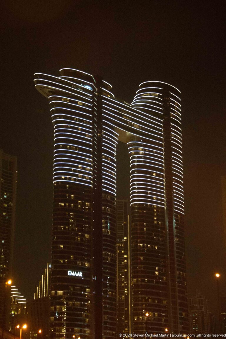 Twin Dubai skyscrapers outlined with horizontal white lights at night.