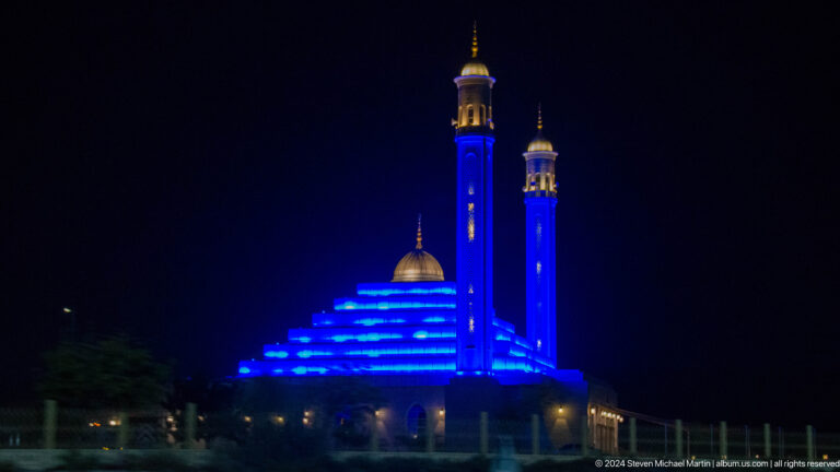 Blue-lit mosque with twin minarets at night in Dubai.
