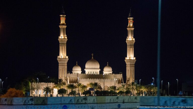 White mosque with multiple domes and two minarets at night.